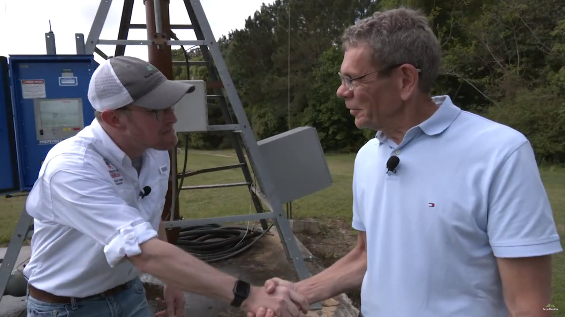 Ranger Nick shakes hands with Dr. George Vellidis in front of a center pivot controller in the field.