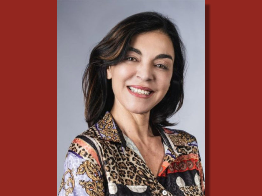 Dr. Stefania De Pascale, wearing a patterned blouse and sporting dark shoulder-length hair, smiles at the camera against a gray background with red borders at the CAES Guest Seminar.