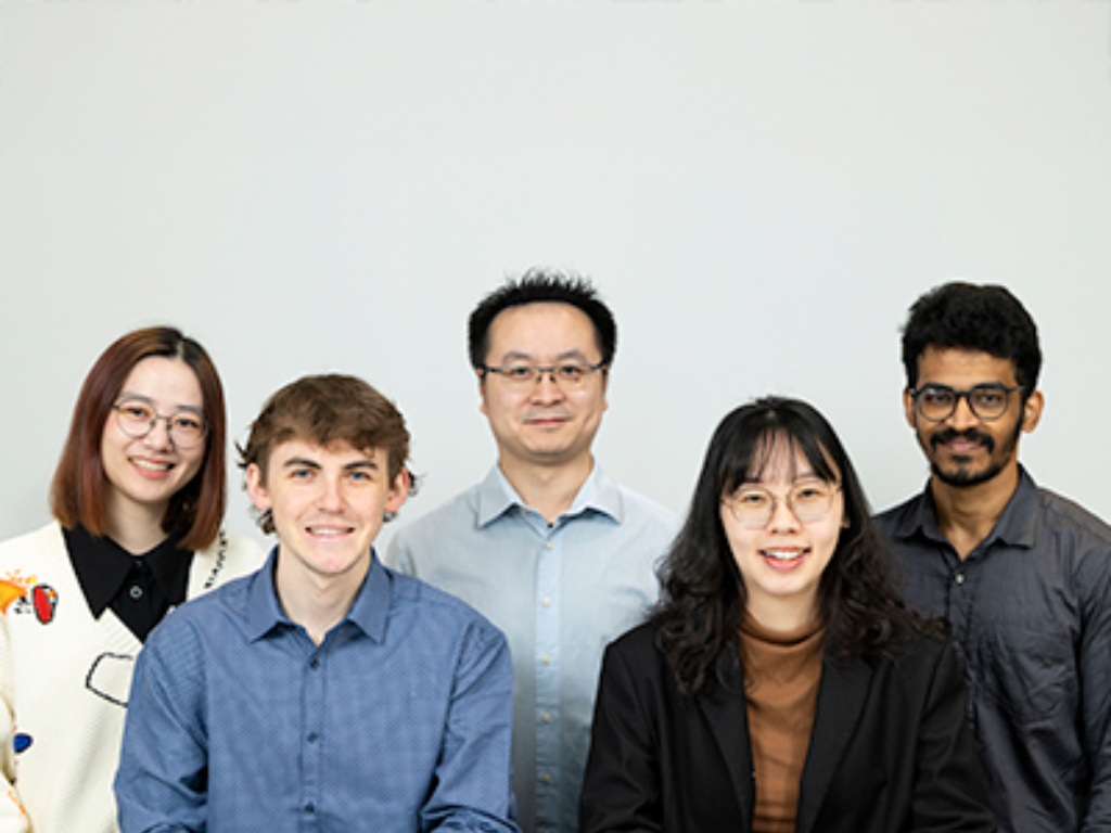Five people, three men and two women, stand and sit together in front of a plain light background, facing the camera and smiling, celebrating their International Collaborative Research Award.