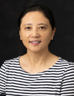 Juliet Chu, wearing a black and white striped shirt, smiles slightly at the camera against a plain dark background.