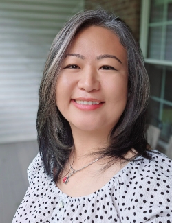 Srijana Thapa Magar, wearing a white polka dot top and a necklace, smiles at the camera in an outdoor setting.