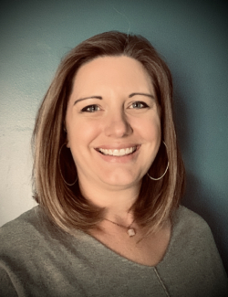 Kelly Gillespie Kelly Gillespie, a woman with shoulder-length light brown hair, wearing hoop earrings and a grey top, smiles in front of a blue wall.