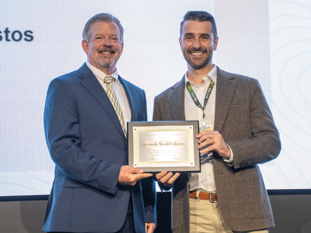 Two men in suits stand side by side smiling, with one holding a framed Teaching Excellence Award plaque that reads Leonardo Morphi Bastos.