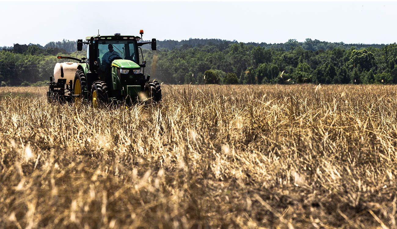 A green tractor driving through a dry field, representing the importance of agriculture to the food supply.